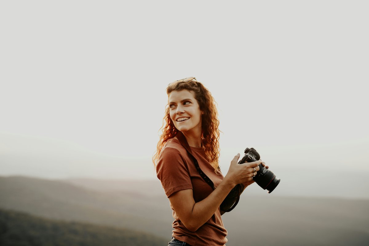 A smiling photographer holding her camera outdoors