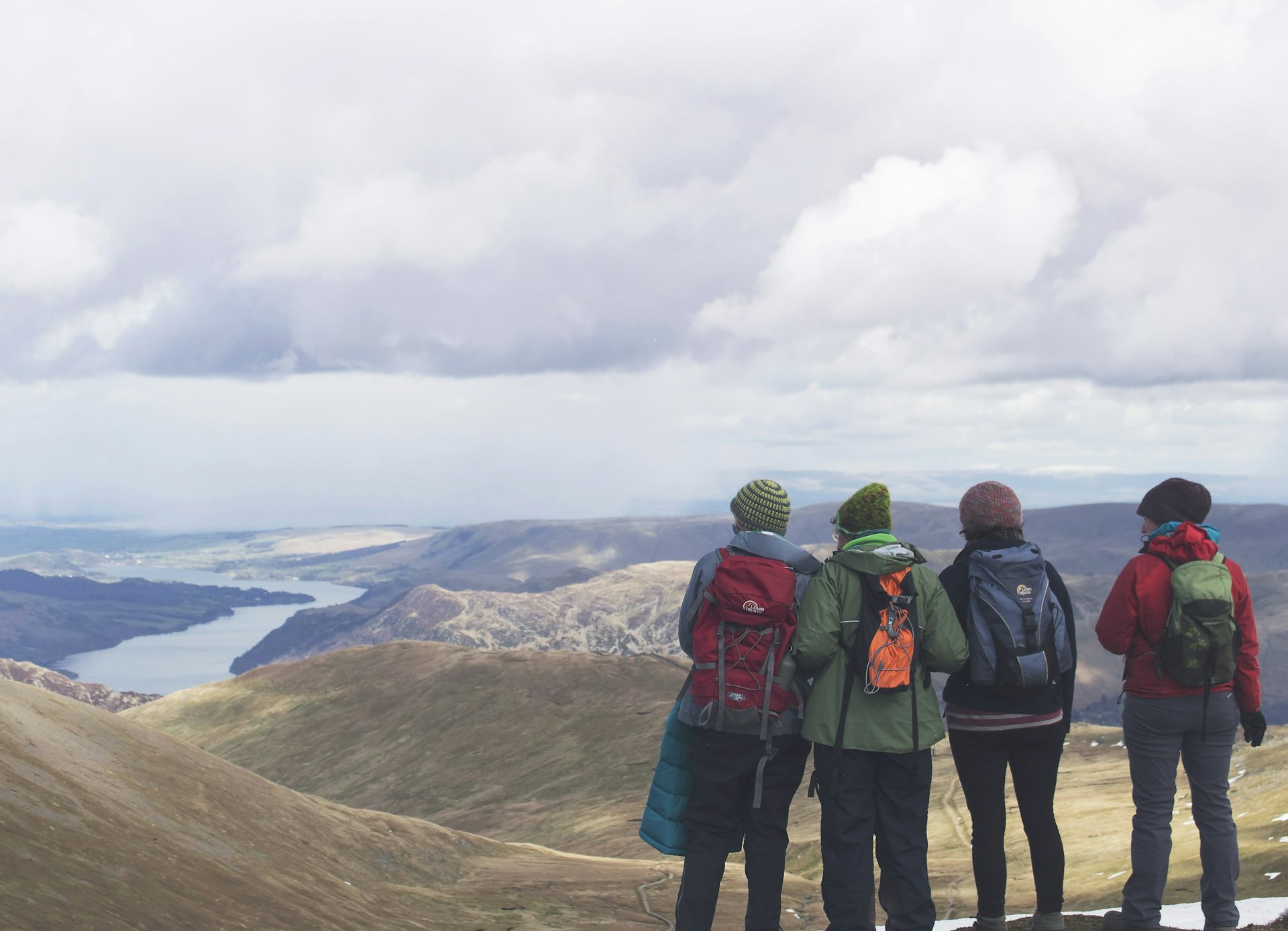 Four friends with backpacks looking out over mountains and a lake