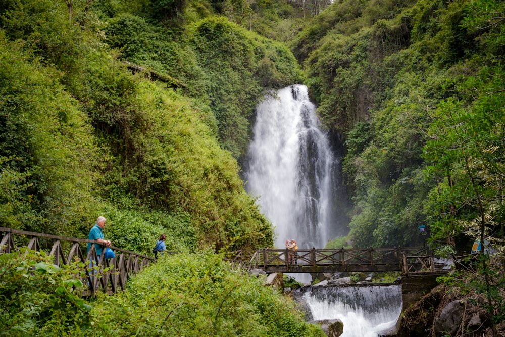 Travelers crossing a bridge beside a thundering waterfall